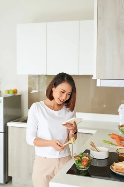 집에서 부엌에서 건강한 샐러드를 요리하는 앞치마를 아름다운 요리하는 전화를 사용하여 — 스톡 사진
