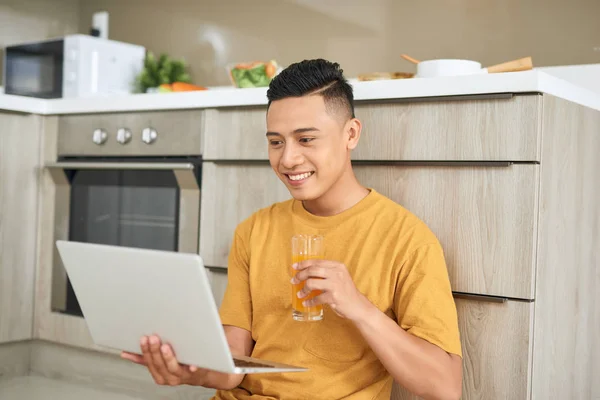 年轻的商人微笑着 吃早饭 在明亮的厨房里用笔记本电脑工作 — 图库照片
