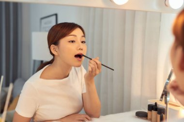 Güzel Asyalı kız makyaj masasında aynada ruj sürüyor.