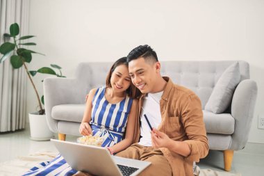 Genç Asyalı çift oturma odasında dizüstü bilgisayardan video izliyor.