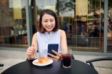 Açık kahve dükkanında, fotokopi çekerken akıllı telefon kullanan güzel bir genç kadının portresi.
