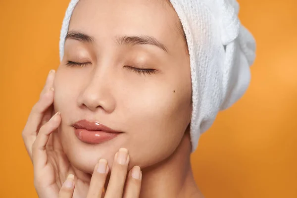 Face of Asian woman smiling and touching her face ,wear towel. Skincare and Cosmetology concept,on orange background