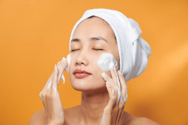 Beautiful model applying cosmetic cream treatment on her face on orange background