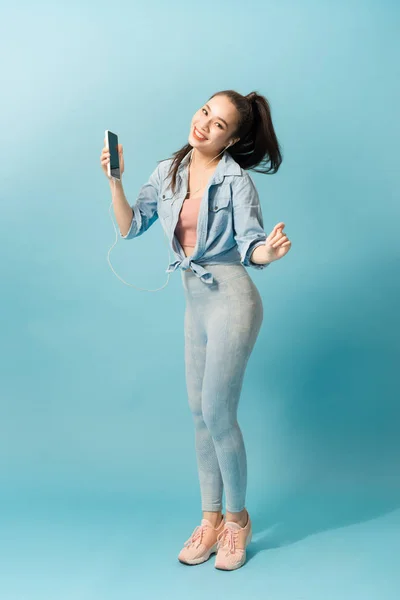 音楽を聴き 青い背景を飛び越えるヘッドフォンで喜び満足アジアの女性 — ストック写真