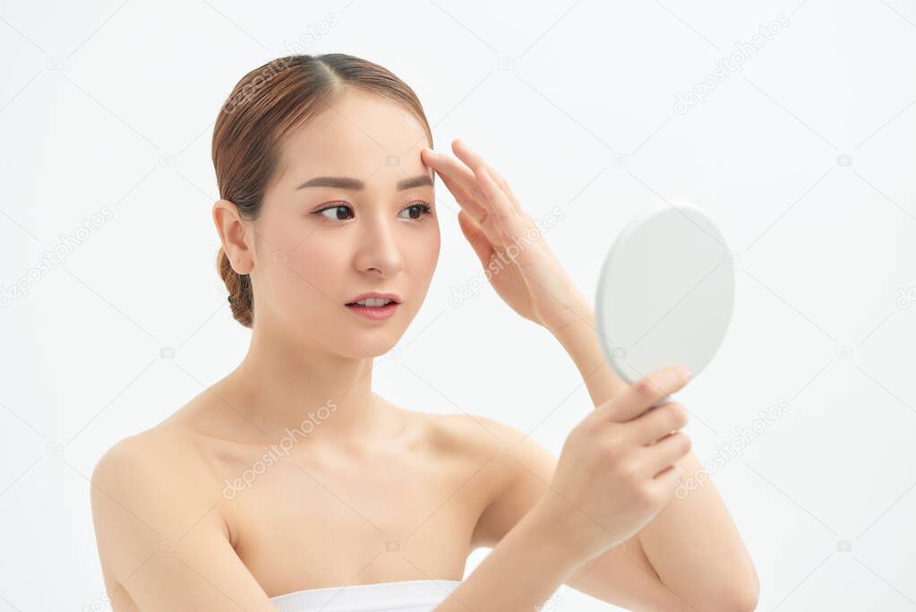 Portrait of young woman with acne problem looking in mirror on white background