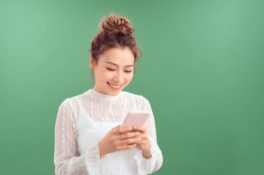 Yeşil arka planda tek başına dururken cep telefonunda yazan mutlu genç güzel..