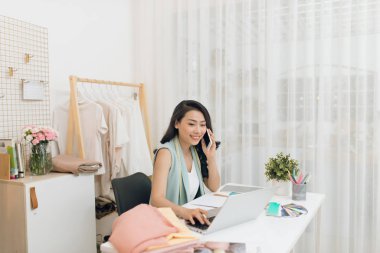 Atölyesinde genç bir Asyalı moda tasarımcısı telefon görüşmesi yapıyor.