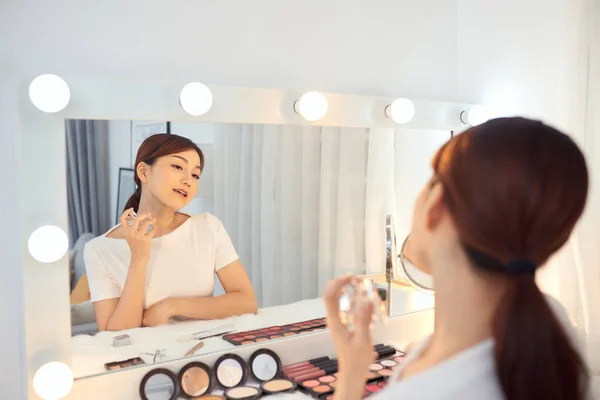 Asian Woman applying fragrance with a spray in front of a make up mirror