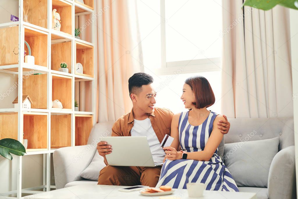 Beautiful Asian Couple Using Bank Card Online With a Laptop at home
