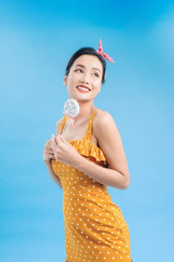 Düşünceli siyah saç modeli mavi arka planda renkli bir lolipop tutuyor.