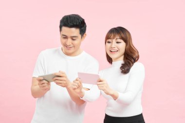 technology and people concept - happy couple in white t-shirts with smartphones over pink background