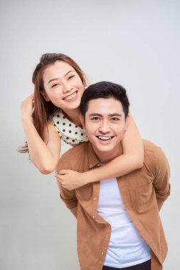 Sonsuza dek aşk. Genç Asyalı yakışıklı erkek arkadaşı sevimli sevgilisini sırtında taşıyor. Saf arka planda günlük kıyafetler giyiyor.