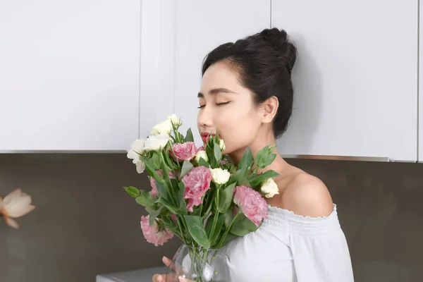 Portrait of young Asian woman with flowers in kitchen.