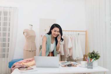 Genç Asyalı moda tasarımcısı / iş adamı laptopunu kullanıyor ve stüdyosunu arıyor.