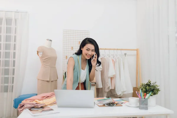 Young Asian fashion designer/business using laptop and calling at her studio