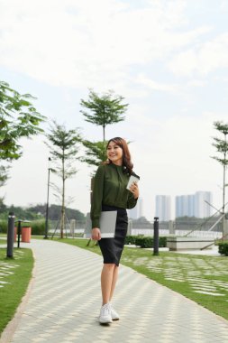 Genç ve başarılı Asyalı bir kadın bir fincan kahve ile işe gidiyor.