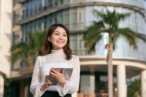 年轻漂亮的女人喝着咖啡 阅读时站在一幢商业大厦外她触摸屏平板电脑 — 图库照片