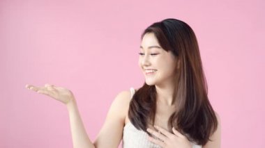 Şirin Asyalı genç kadın moda makyaj jest elle pink izole bir şeyler gösteriyor.