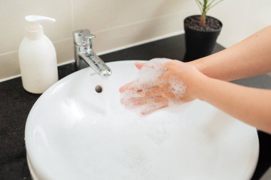 Suyun altında sabunla ellerini yıkamak..