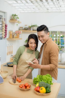 Güzel genç çift evde yemek pişirirken cep telefonu kullanıyor ve gülümsüyor.