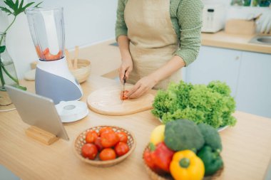 Mutfakta tablet bilgisayar kullanan ve sebze salatası pişiren genç bir bayan resmi