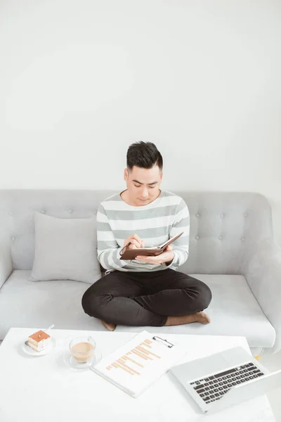 Asian Man Writing Notebook Sitting Sofa Home — Stock Photo, Image