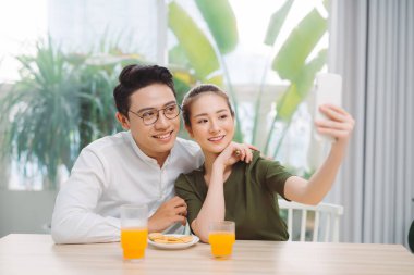 Güzel genç bir çift selfie çekiyor, akıllı bir telefon kullanıyorlar ve dairelerinde otururken gülümsüyorlar.