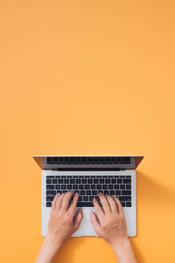 Düz dizüstü bilgisayar, kahve ve sarı arka planda defter. Klavyede yazan erkek elleri