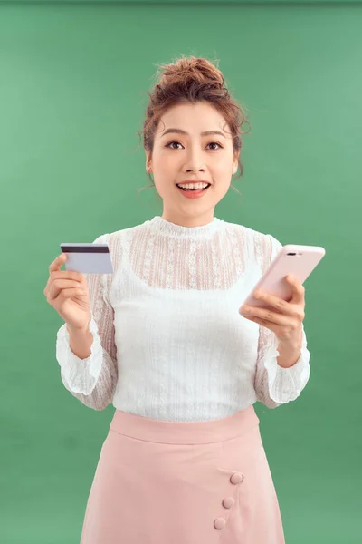 Возбужденная Молодая Азиатка Изолирована Зеленом Фоне Помощью Мобильного Телефона Кредитной — стоковое фото