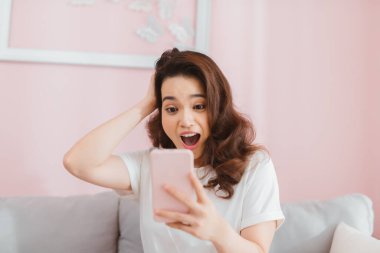 Şaşırdım, güzel Asyalı kanepede dinleniyor ve telefonunu oturma odasında kullanıyor.