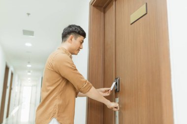 Genç bir adam, bir odanın elektronik sensörünün önünde bir anahtar kartı tutuyor.