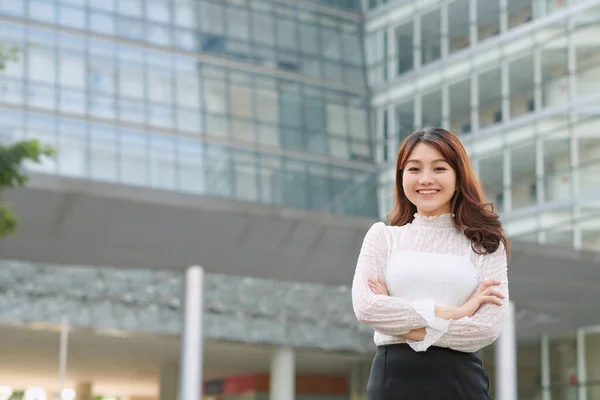 Spacious portrait of an attractive young executive business woman in a city street, smiling with crossed arms outdoors.