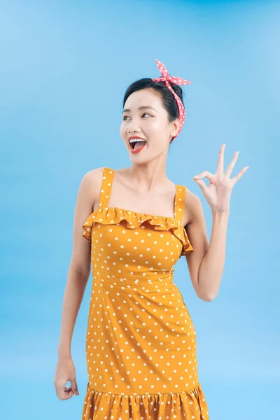 portrait of a beautiful woman pinup retro style pointing at you smiling laughing isolated blue background wall. Body language, gestures, psychology.