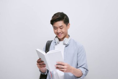 Asyalı üniversite öğrencisinin belden yukarı portresi kitap okumaktan alıkoyuldu ve beyaz arka planda izole edilmiş, geniş bir gülümsemeyle kameraya baktı.