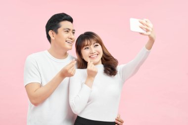 Birlikte mutlu anları yakalayın. Mutlu genç çift, gri arka planda dururken özçekim yapıyor ve gülümsüyor.