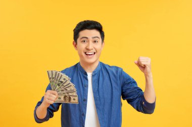 Heyecanlı, şaşkın, şen şakrak menajerin portresi sarı arka planda izole bir sürü banknot gösteriyor.