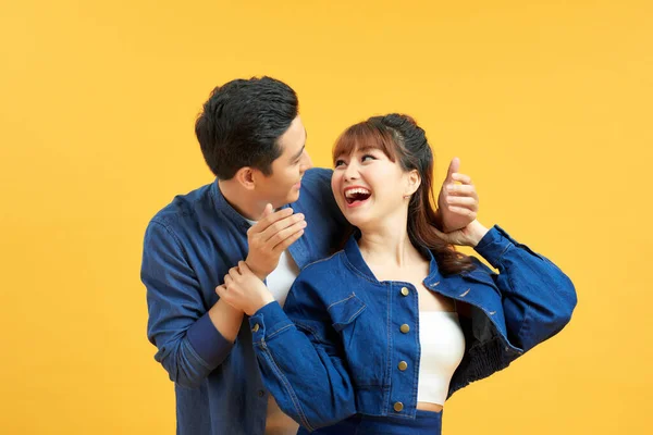 Couple playing hide and seek. Man standing behind his wife and closing her eyes, yellow background