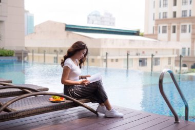 Otelde yüzme havuzunun arkasında kitap okuyan güzel bir Asyalı kadın..
