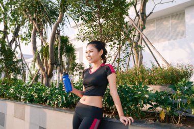 Elinde su şişesi olan güzel bir kadın koşucu. Spor salonundaki kadın dışarıda antrenman yaptıktan sonra ara verdi..