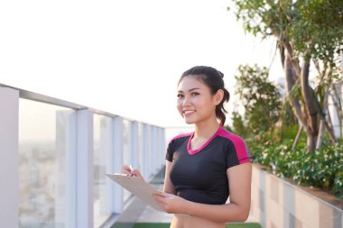 Dişi Asyalı antrenör dışarıda fitness sınıfıyla birlikte panoya yazı yazıyor..