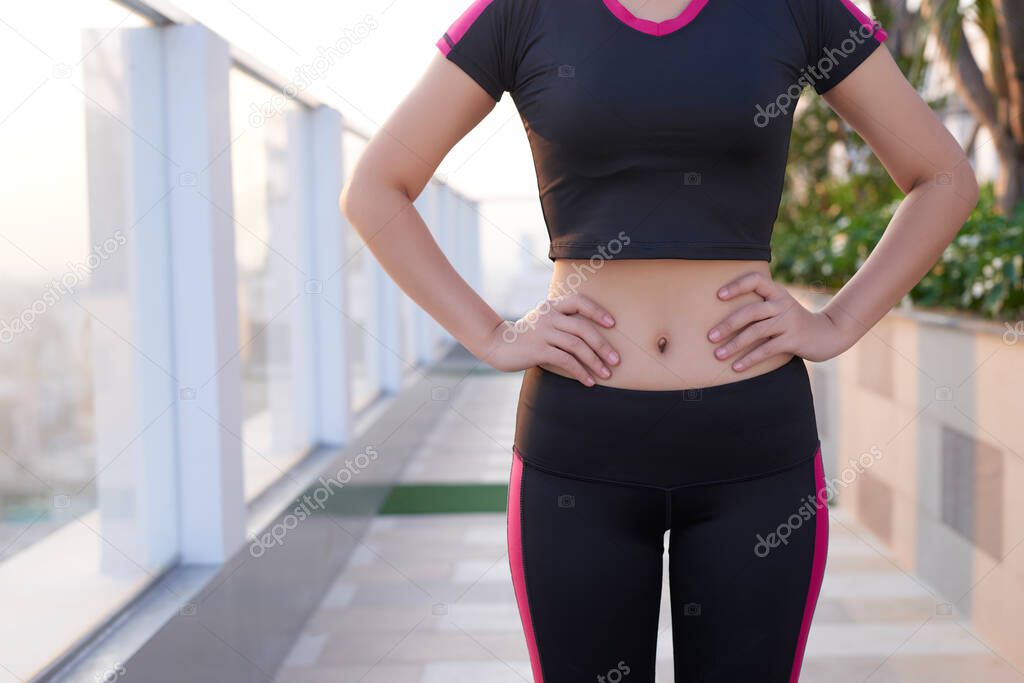 Close up of fit woman's torso with her hands on hips.