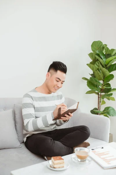 Asiático Homem Escrevendo Notebook Quando Sentado Sofá Casa — Fotografia de Stock