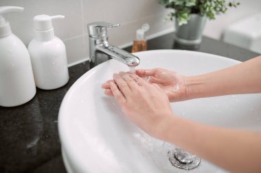 Yıkama. Kadın musluk suyunun altında ellerini yıkıyor banyo musluğunun altında akan suyla ellerini yıkıyor. Hijyen
