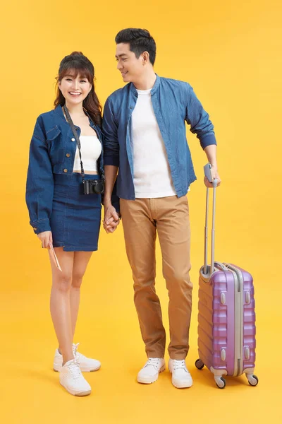 Traveler asian couple with backpack and suitcase standing isolated over yellow background. Couple Asian going to summer vacation. People, active lifestyle, relaxation and joy concept. Happy couple.