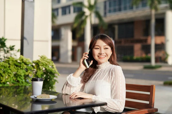 Young and beautiful Asian freelance business woman using a smart phone at the restaurant terrace in the urban city