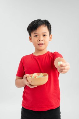 Beyaz arka planda renkli şekerleri ve jöleli şekerlemeleri olan gülümseyen çocuk.