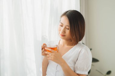 Elinde bir bardak sıcak çayla pencerenin yanında duran güzel bir kadın. Öğleden sonra çay konsepti.