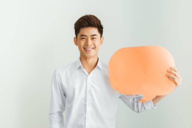 Genç Asyalı adam beyaz arka planda boş konuşma balonu tutuyor.