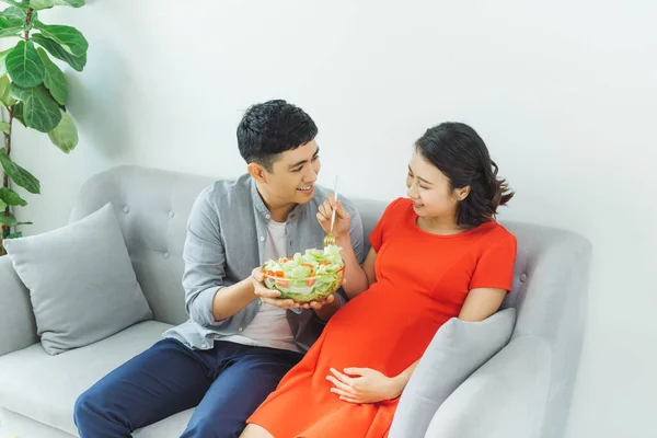 素敵な若い妊娠カップル女性の健康的な朝食を持っていること 一緒にソファでリラックス — ストック写真