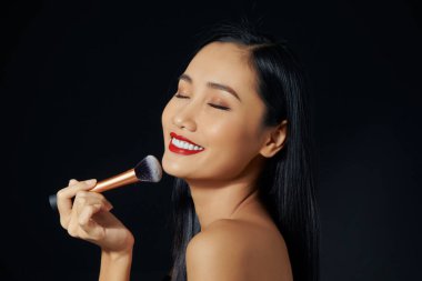 Güzellik Surat. Gülümseyen güzel bir kızın portresi. Yüzü allık sürerek kozmetik fırçayla kızarıyor..